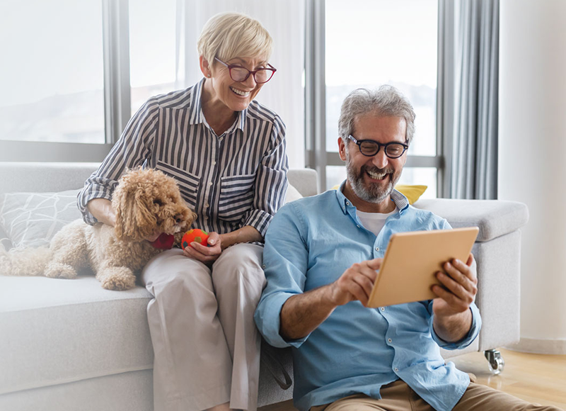 Senior couple sitting on the couch looking at a tablet.