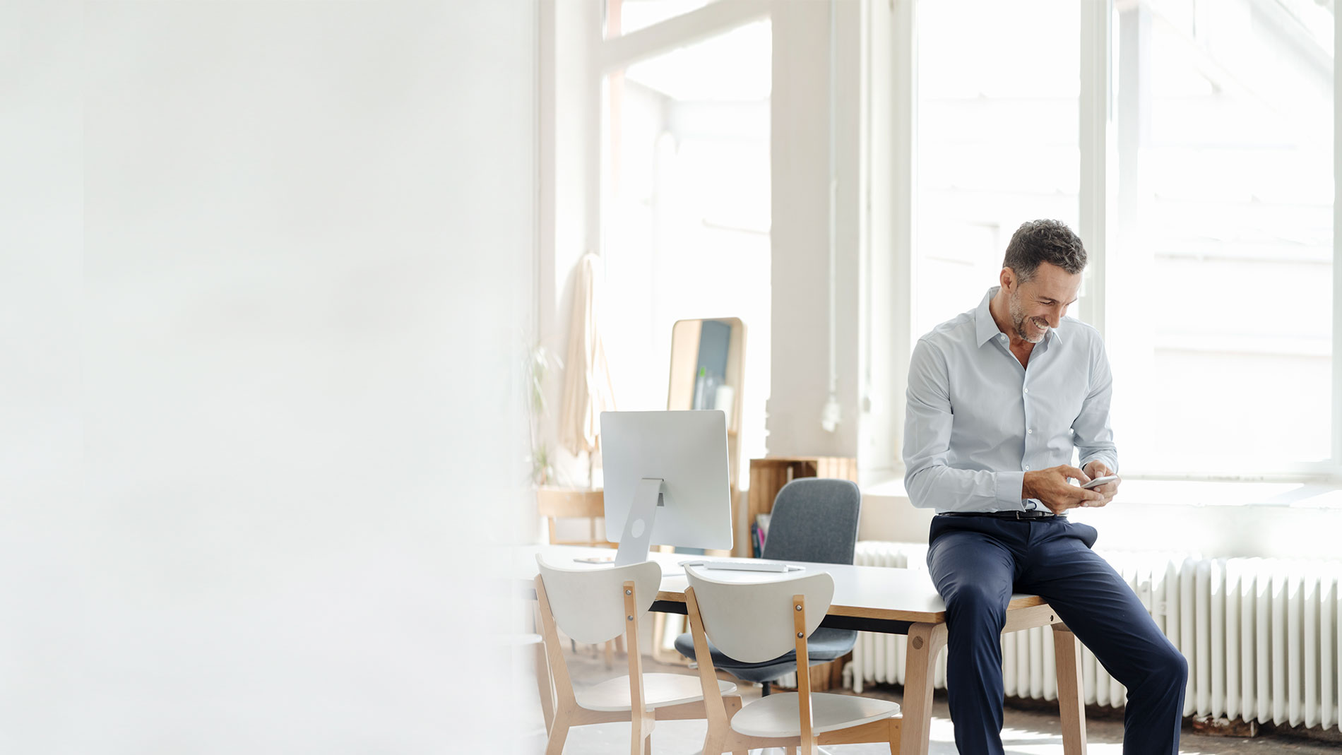 Man standing next to his desk looking at his mobile phone.