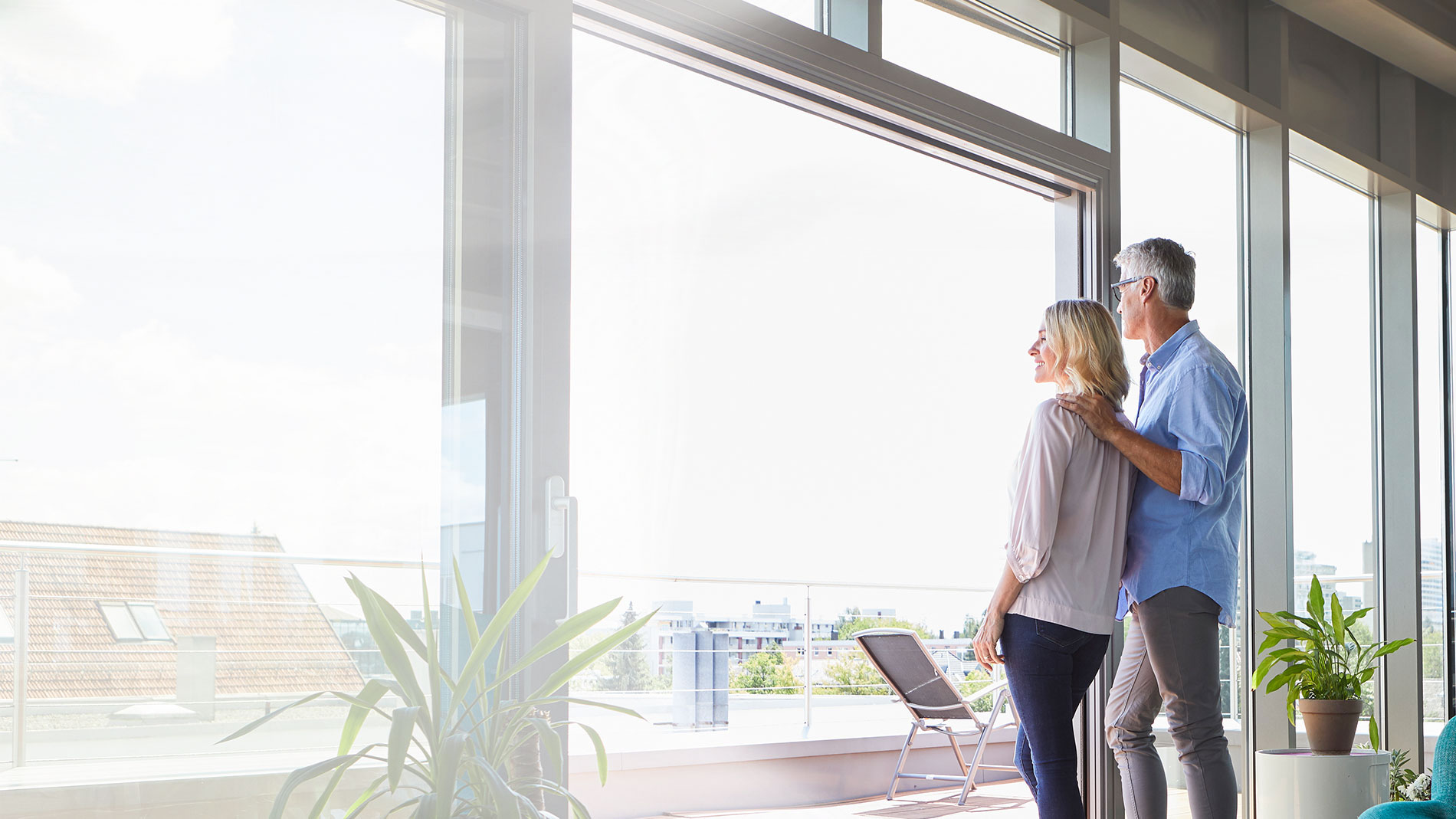 Older couple standing in front of their condo window and looking at their view.