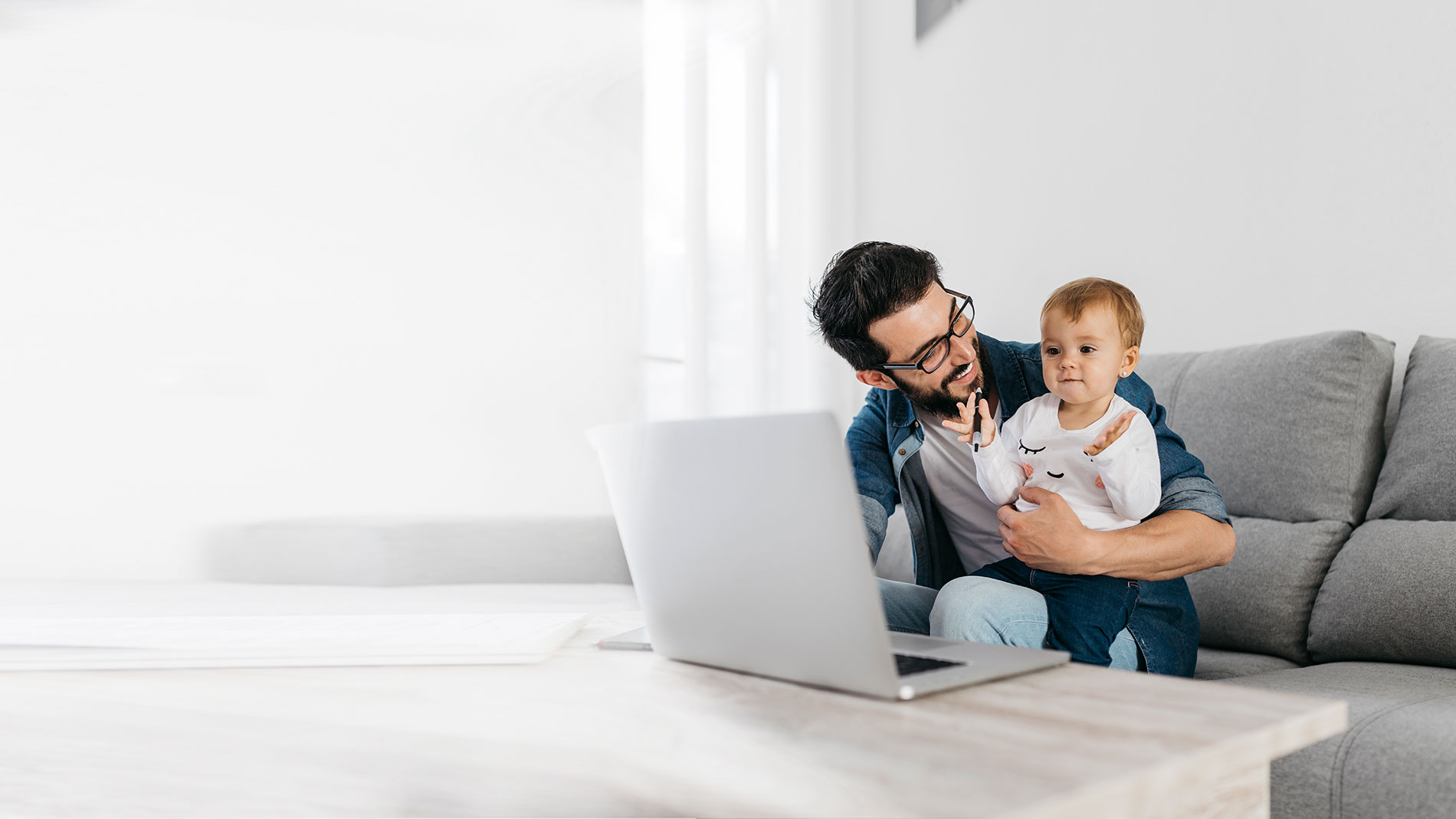 Father and baby daughter sitting on the couch working on laptop.