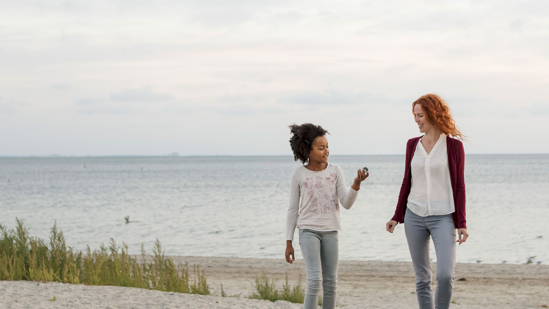 Mom walking with young daughter on the beach.