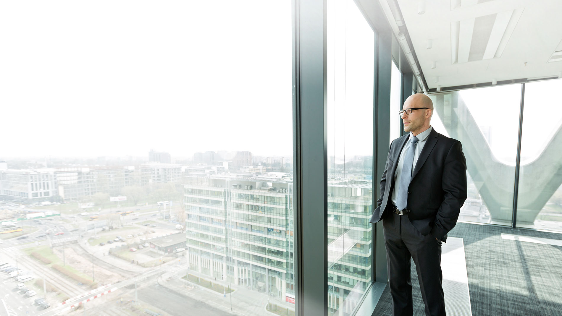 Man looking out of his high rise office at the city buildings.