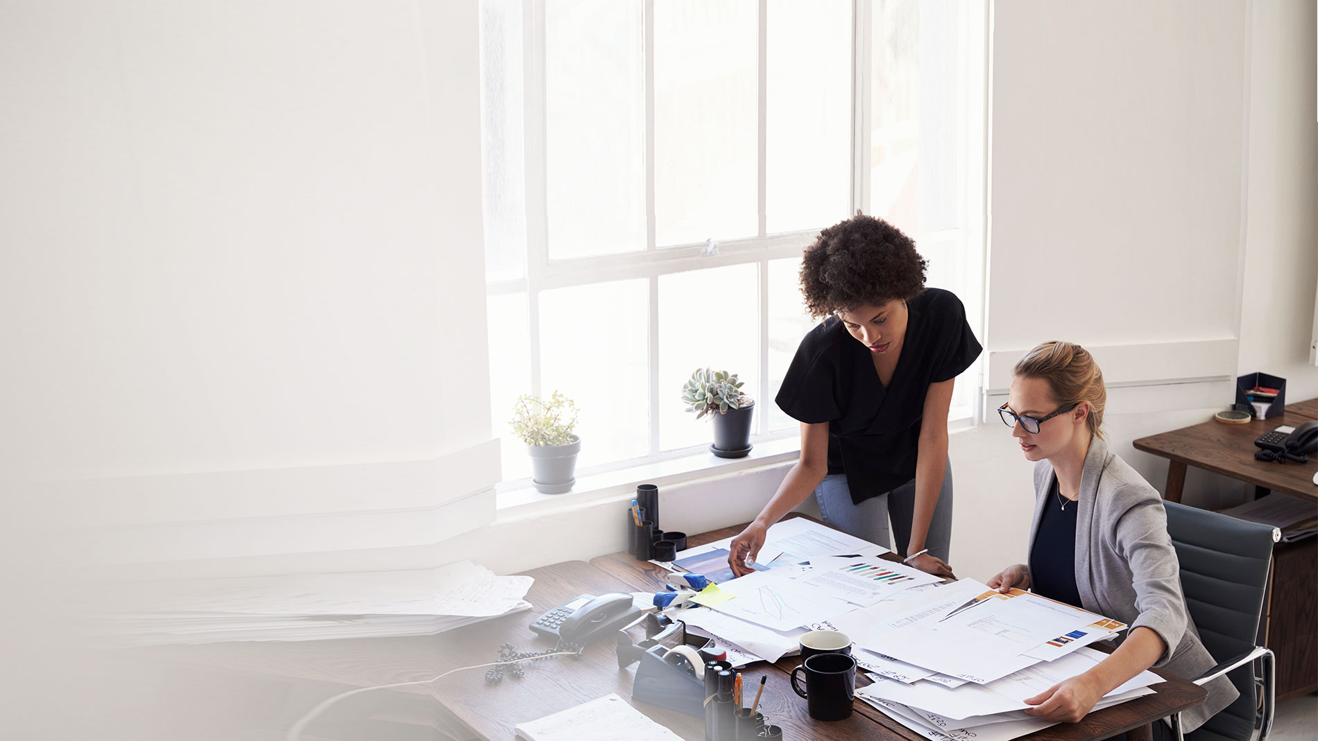 Women working at a desk full of paperwork.