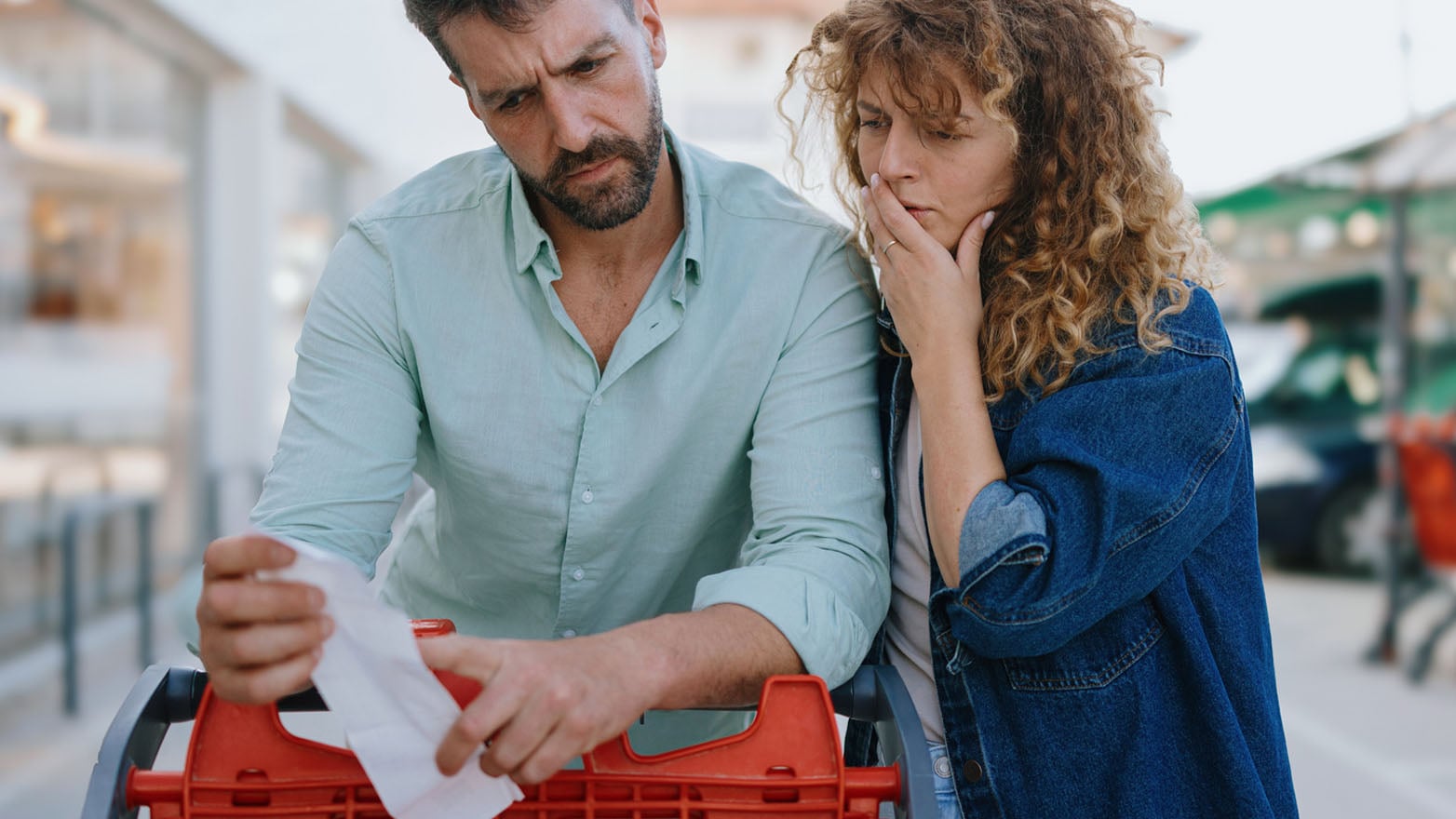 Two people reviewing a receipt at a shopping cart, representing inflation fatigue and the challenge of managing rising costs.