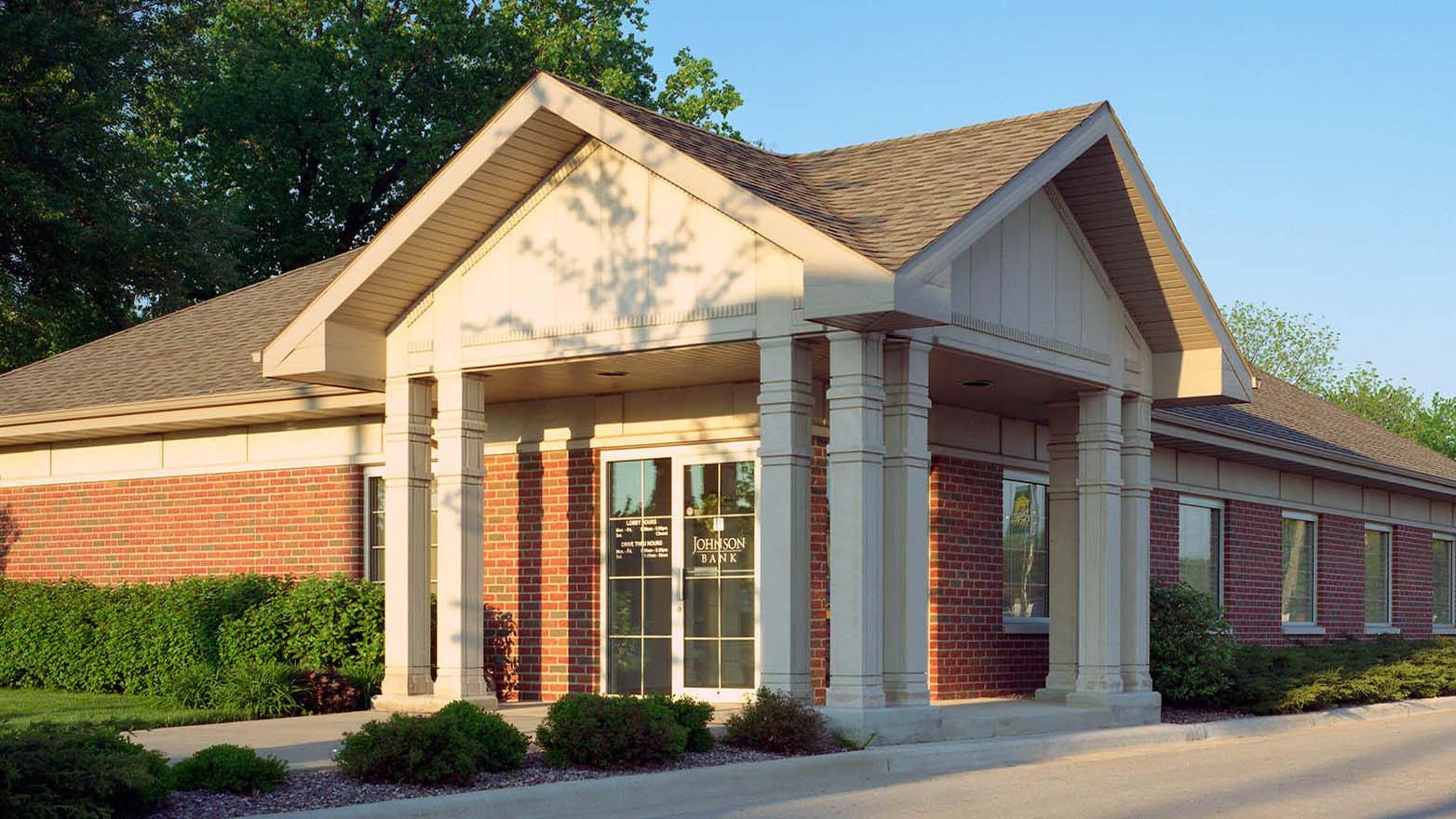 Exterior of the Johnson Financial Group building with gray brick, light wood siding, and a covered drive-thru, under a partly cloudy sky.