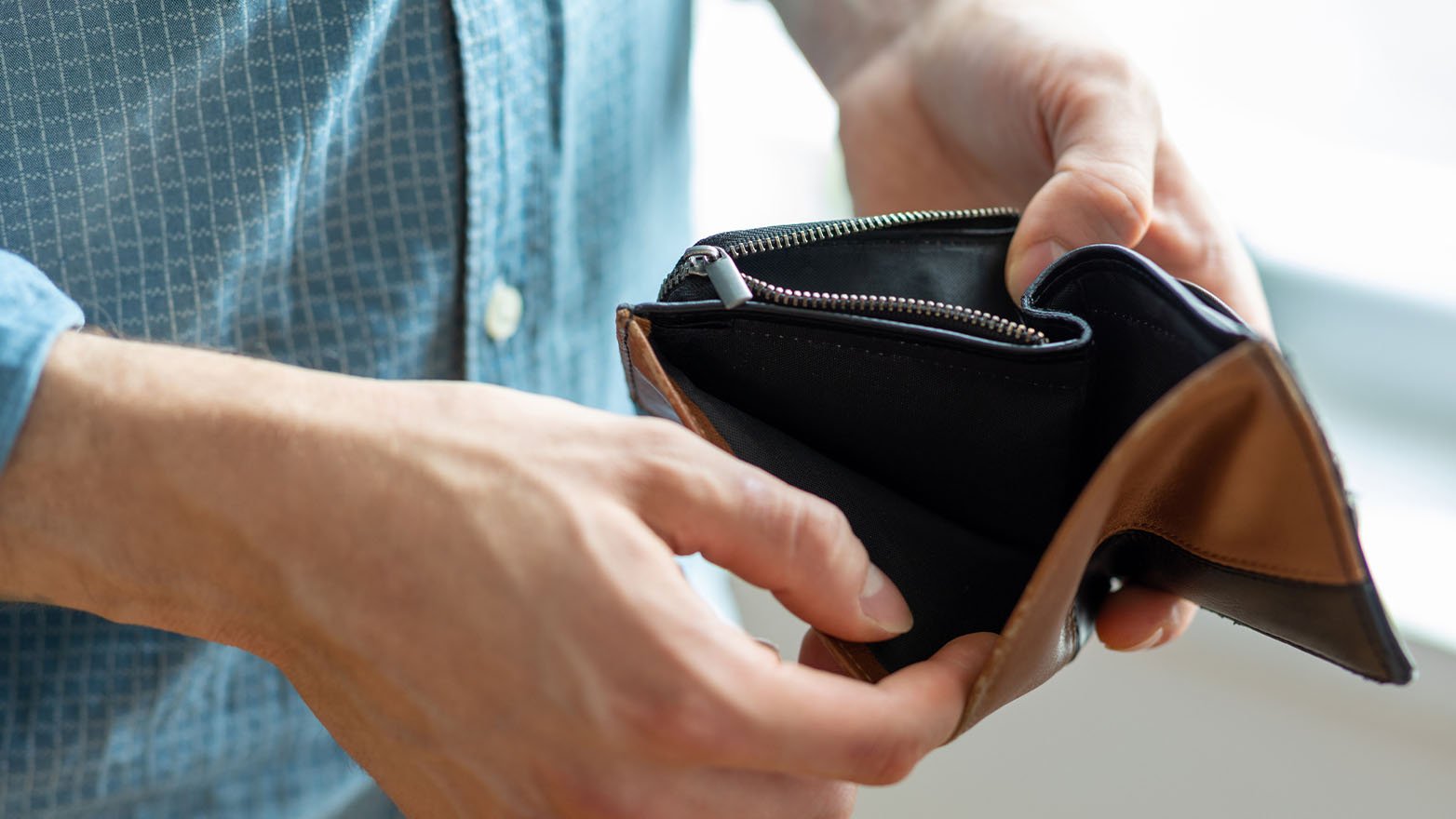 Hands hold an open, empty black and brown wallet.