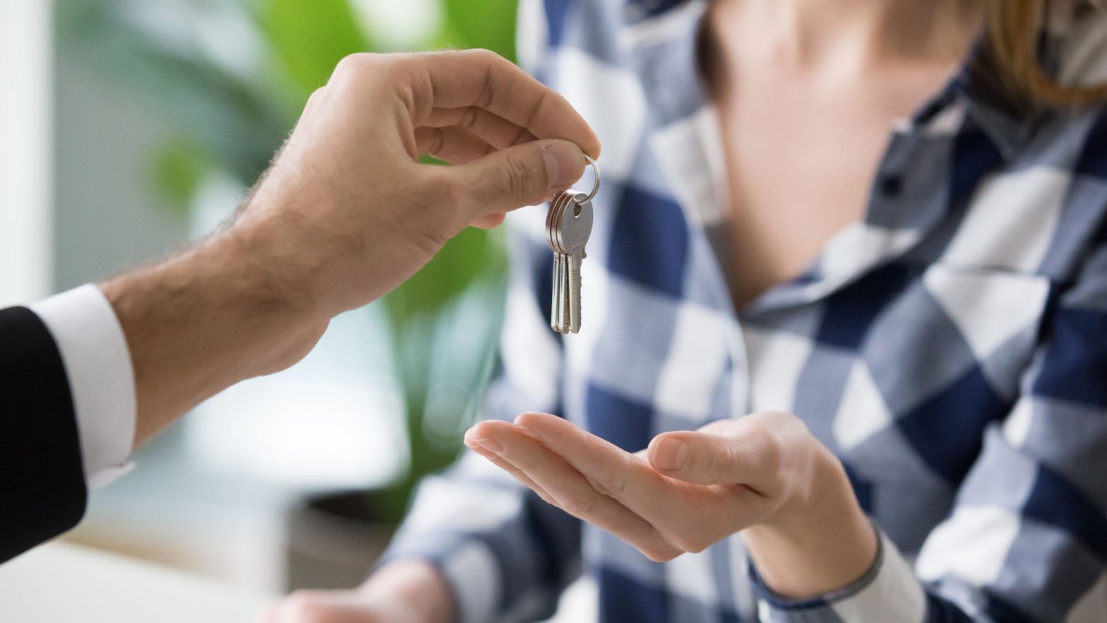 Close-up of one person handing a set of house keys to another person with an open hand.