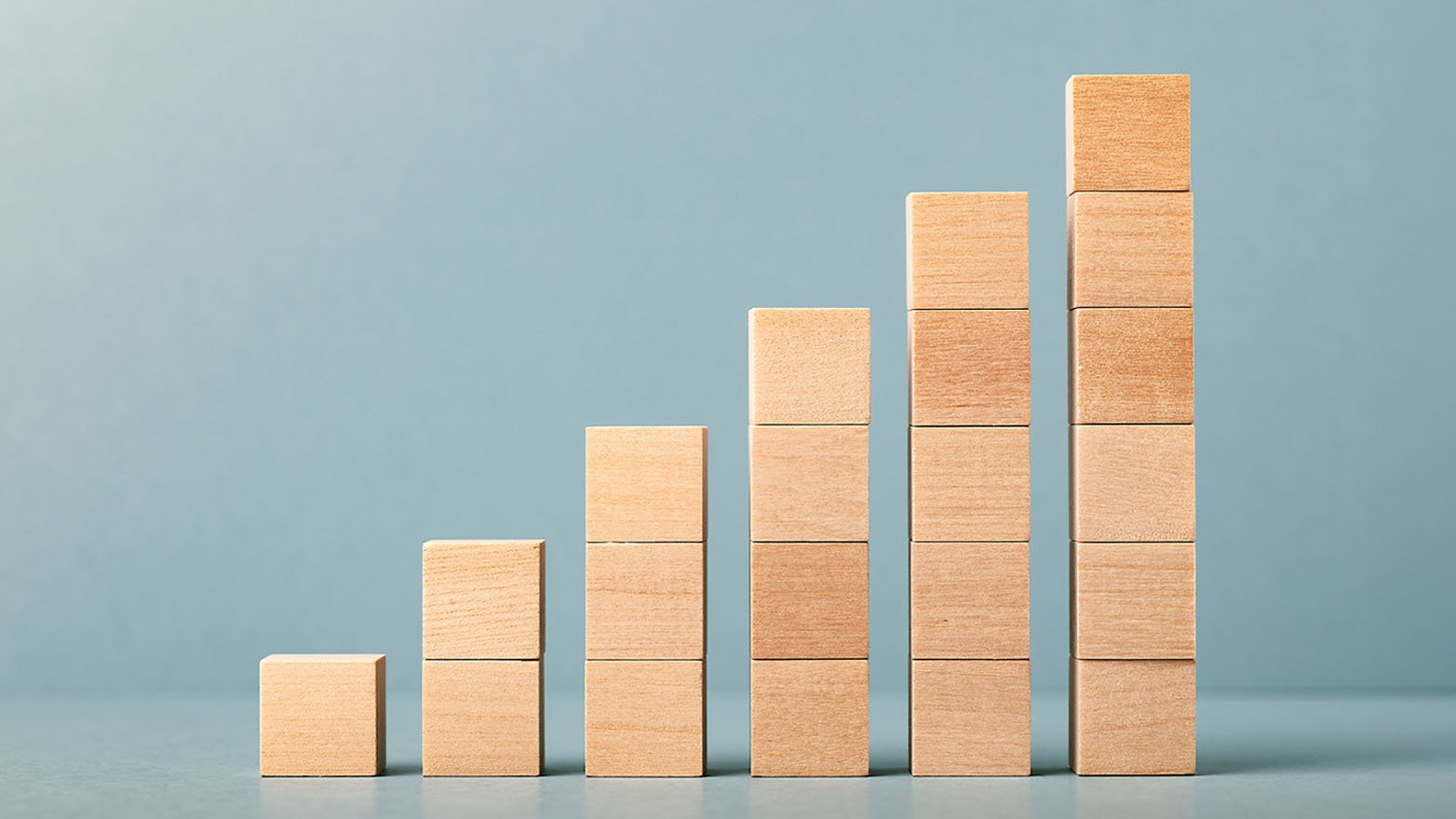 Stacked wooden blocks in ascending order, from shortest to tallest, symbolize gradual growth and progress.