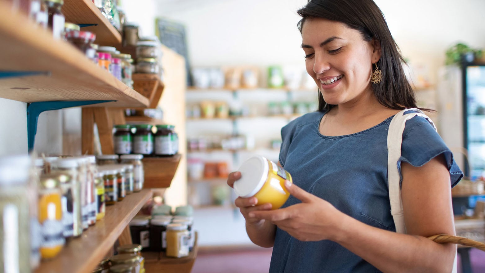 Woman browsing jars on a small shop shelf, smiling as she checks a product label—highlighting the experience of shopping local in Wisconsin.