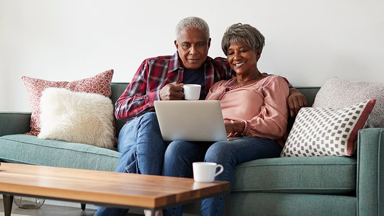 senior couple on couch using laptop