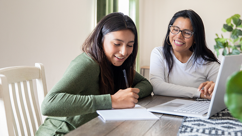mother and daughter sitting in a kitchen at the table looking at paperwork.