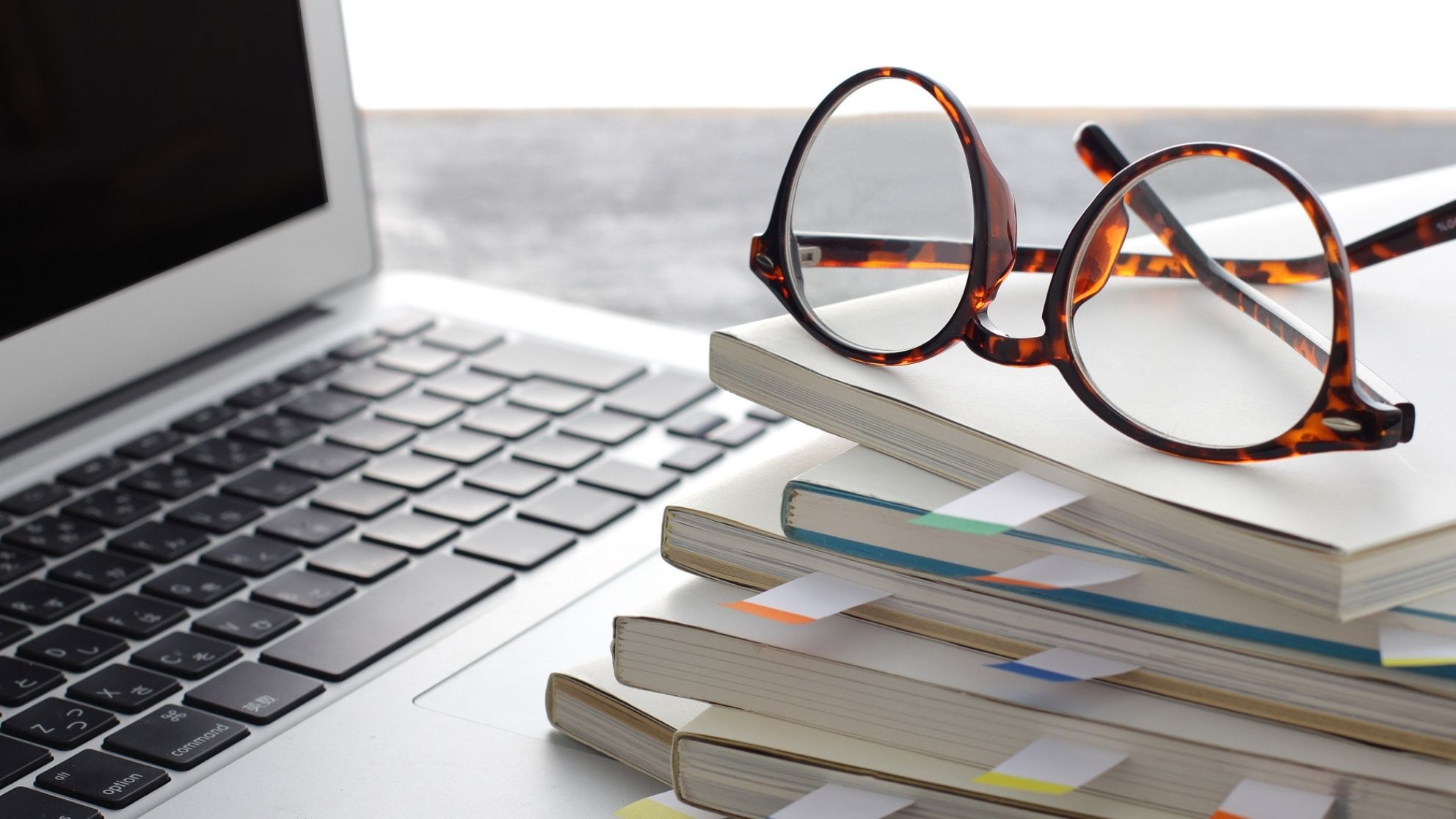 Close-up of a laptop computer with a pair of reading glasses and a stack of textbooks beside it.