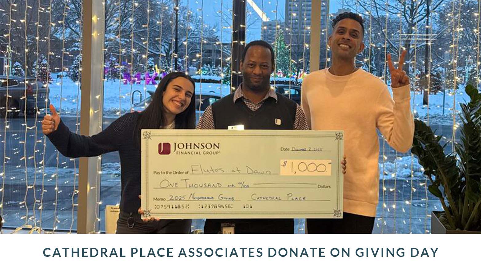 Three people standing indoors holding a large ceremonial check, with decorative lights visible in the background. Caption below reads “Cathedral Place associates donate on Giving Day.”