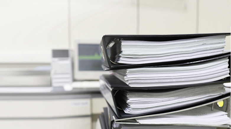 A stack of full binders on a desk.