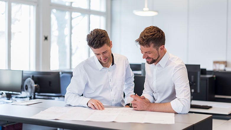 Two male co-workers sitting at a desk reviewing paperwork.