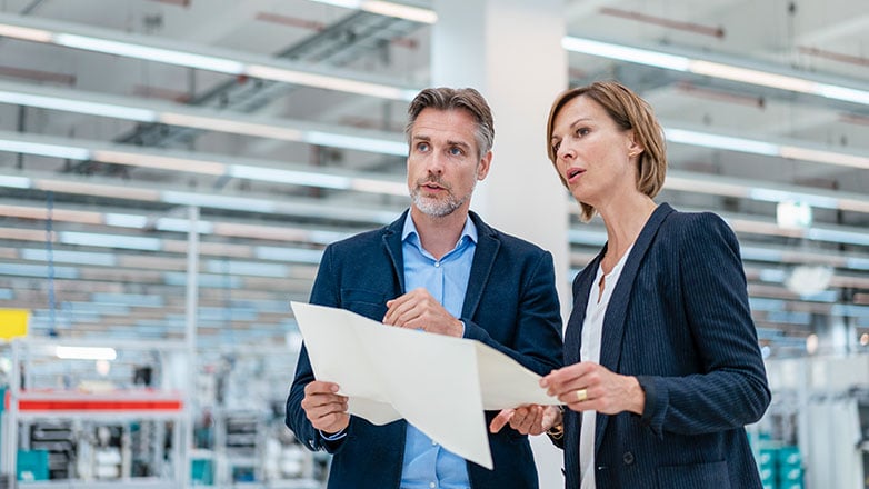 A female and male business owner standing in new warehouse discussing plans to remodel.