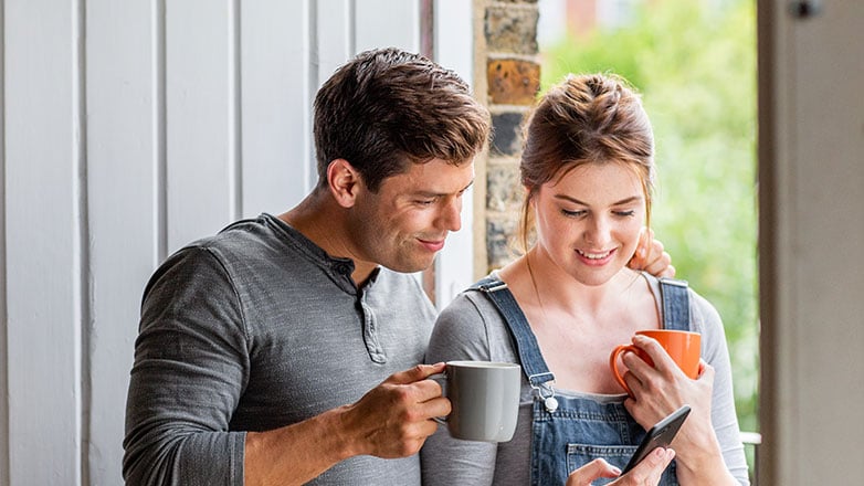 Young couple standing by window and looking at their mobile phone.