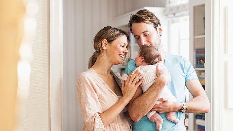 Couple standing in there home with their newborn baby.