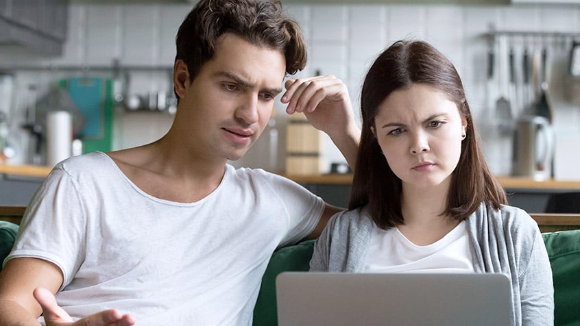couple looking at a computer with concerned looks on their faces.