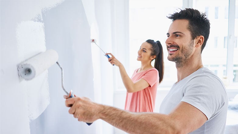 Couple smiling as they paint the walls in their new home.