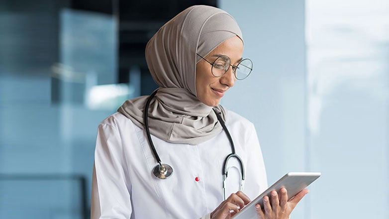 A young physician reviews notes on a tablet.