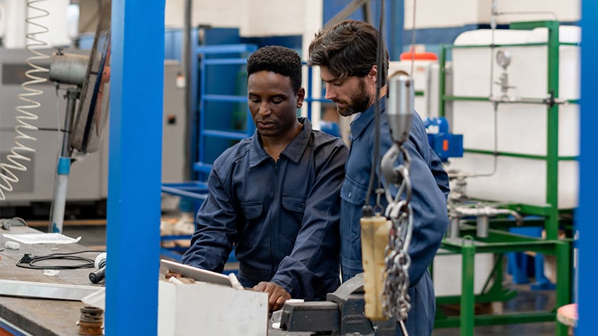 male factory worker teaching another male factory worker on the job