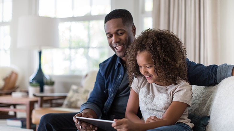 Dad and daughter sitting on the couch watching and ipad.