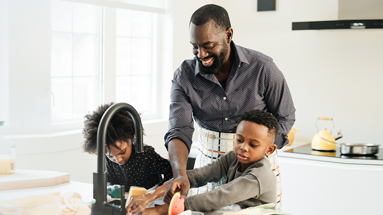 african american dad washing dishes with kids after a meal.
