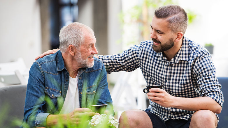 Father and son have a cup of coffee together on the porch.