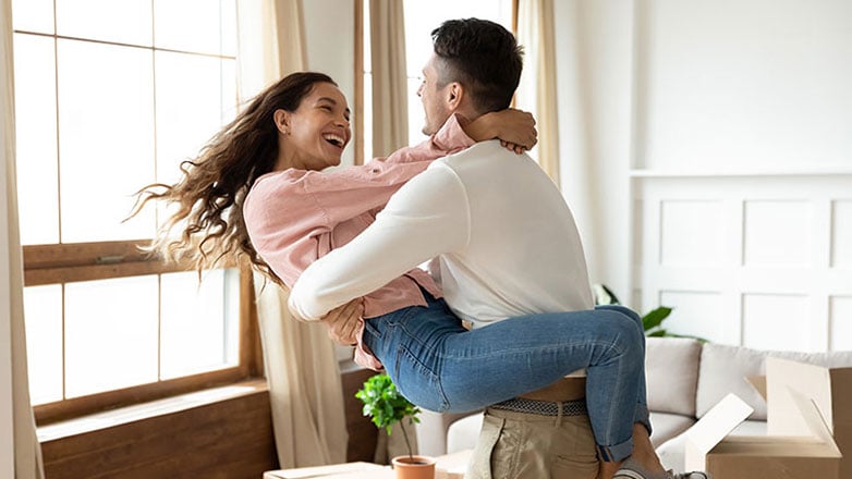 Husband happily twirls his wife around in the living room of their new home.