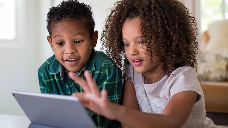 A young brother and sister look at a tablet together.