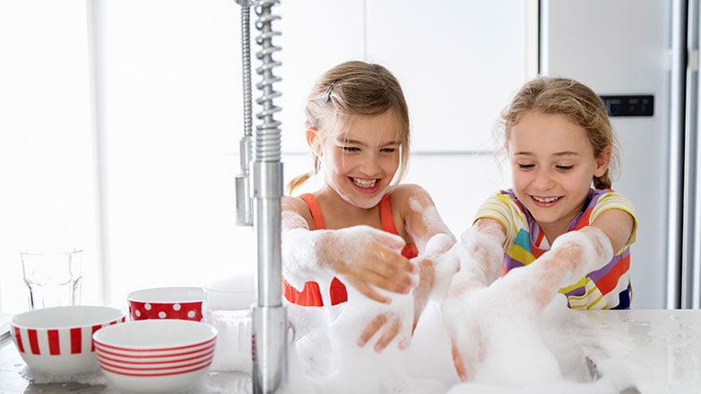 Sisters having fun washing dishes in their home.