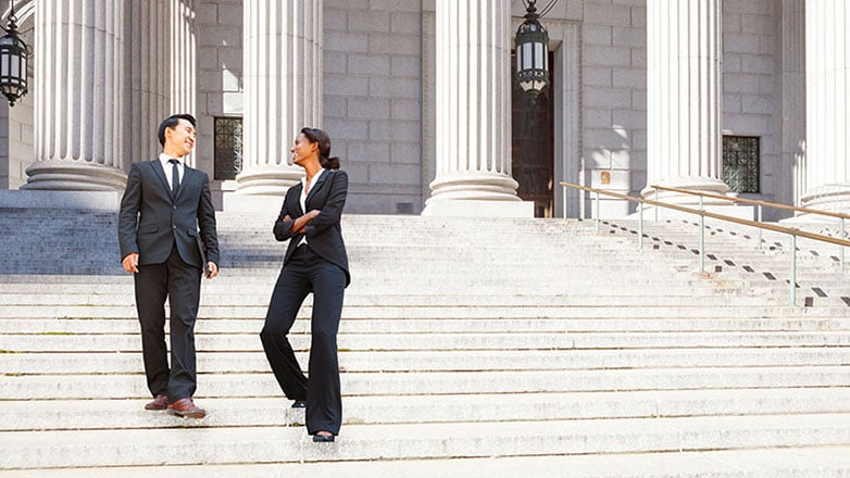 Two lawyers walk down the steps of a courthouse.