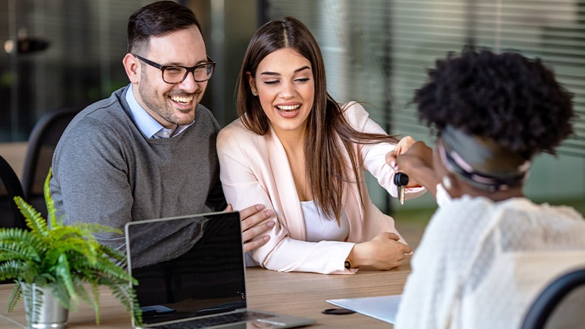 mortgage lender handing a couple their house key.