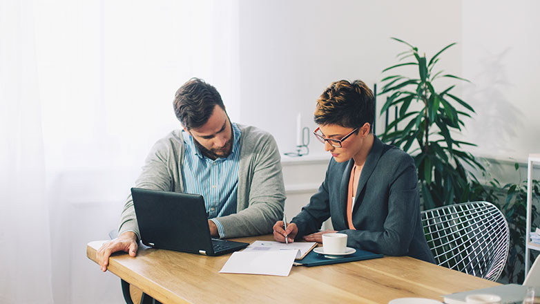 Male and female looking through paperwork at a desk.