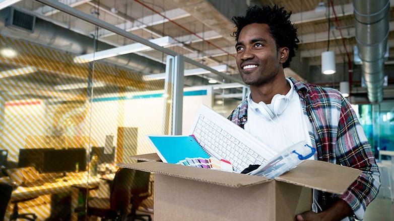 Young man carries his box of office supplies into his new workplace.