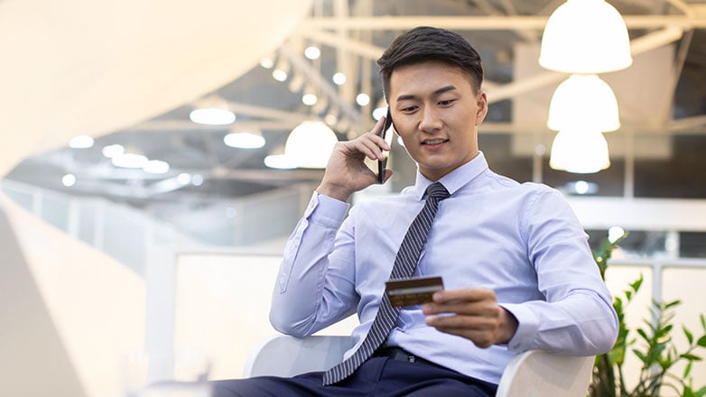 Man sitting at his desk using a credt card to make a purchase.