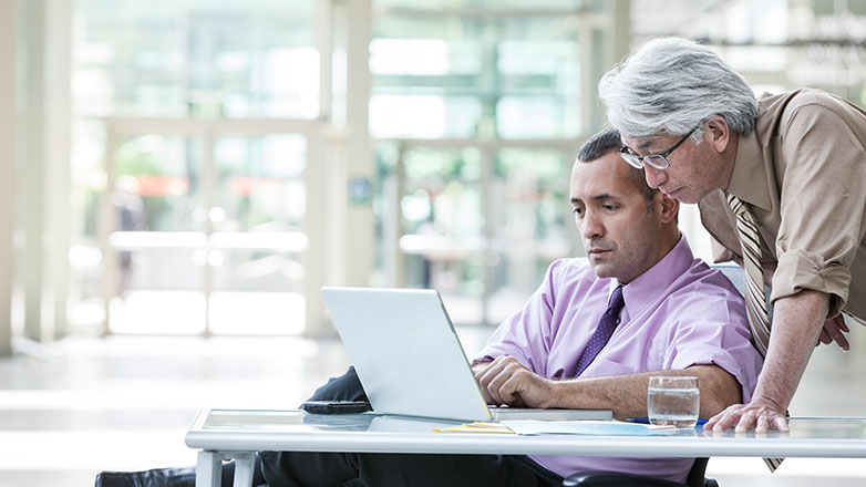 Two men at a table looking at a laptop computer.