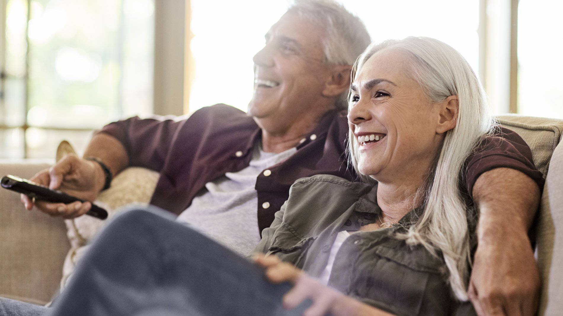 middle aged couple sitting on the couch laughing with each other.