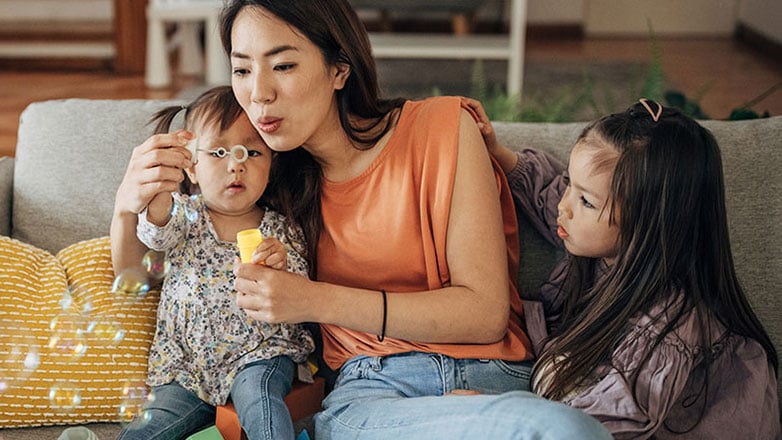 Mom blows soapy bubbles to entertain her two toddler daughters.