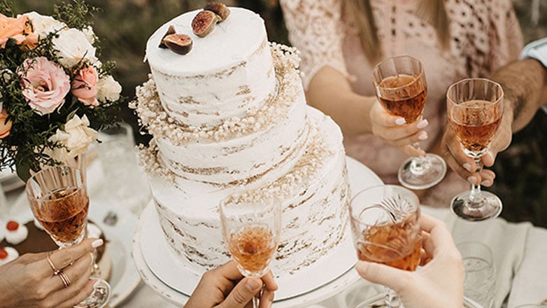 Wedding guests gather around a wedding cake and hold glasses of champagne.