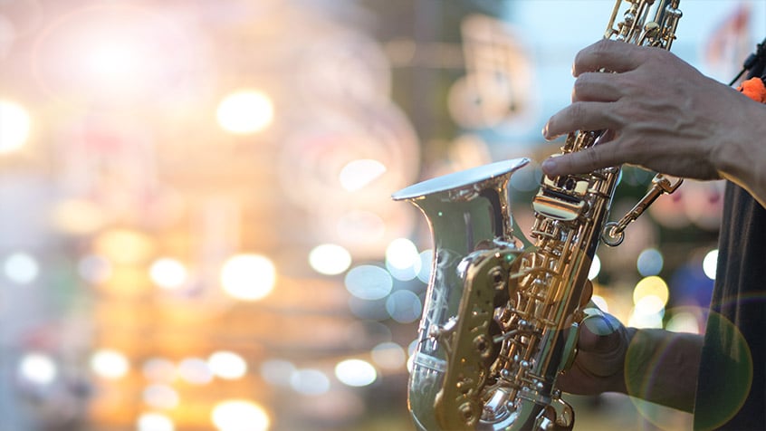 close up of a man holding a saxophone with twinkling lights in the background.