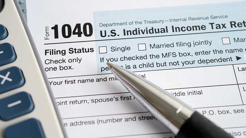 A US 1040 tax form with a calculator and a pen laying on top of it. The "Single" filing status checkbox is in focus.
