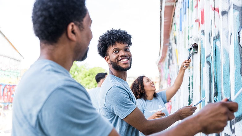 Volunteers paint over grafitti on a building.