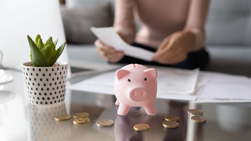 close up of a piggy bank with a woman looking at paperwork in the background