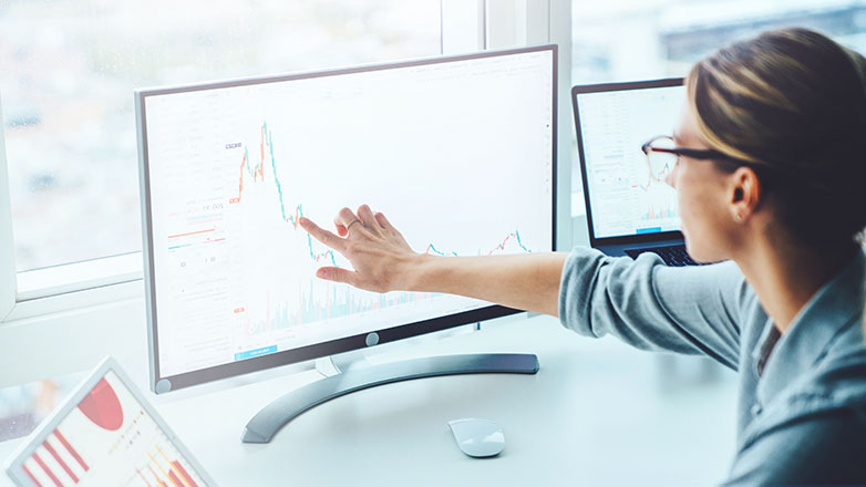Woman sitting at her desk pointing to her monitor while looknig at reports.