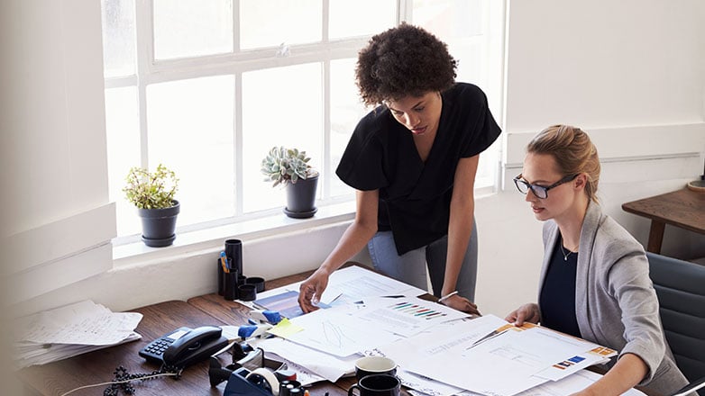 Women working at a desk full of paperwork.