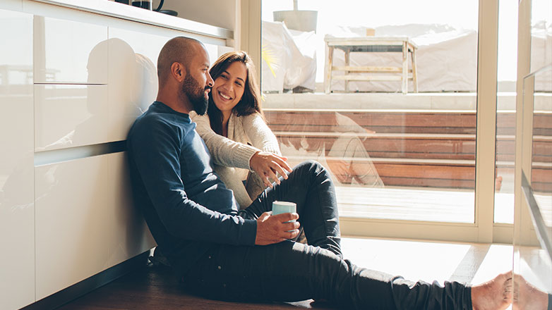 Couple sititng on their kitchen floor drinking coffee and talking.