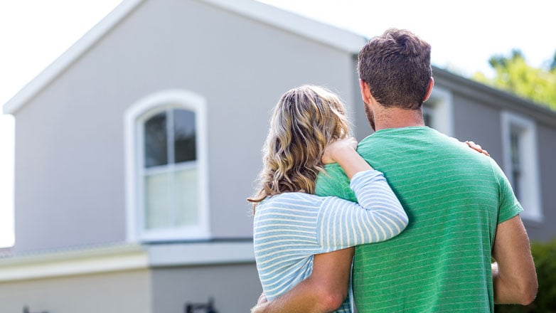 couple holding arms looking away towards house
