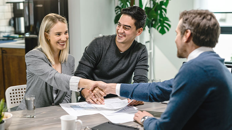 couple shaking hands with banker at desk with construction plans